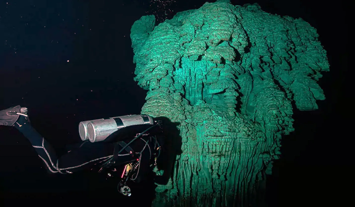 Diver examining a large illuminated limestone formation in Kin Ha cenote.