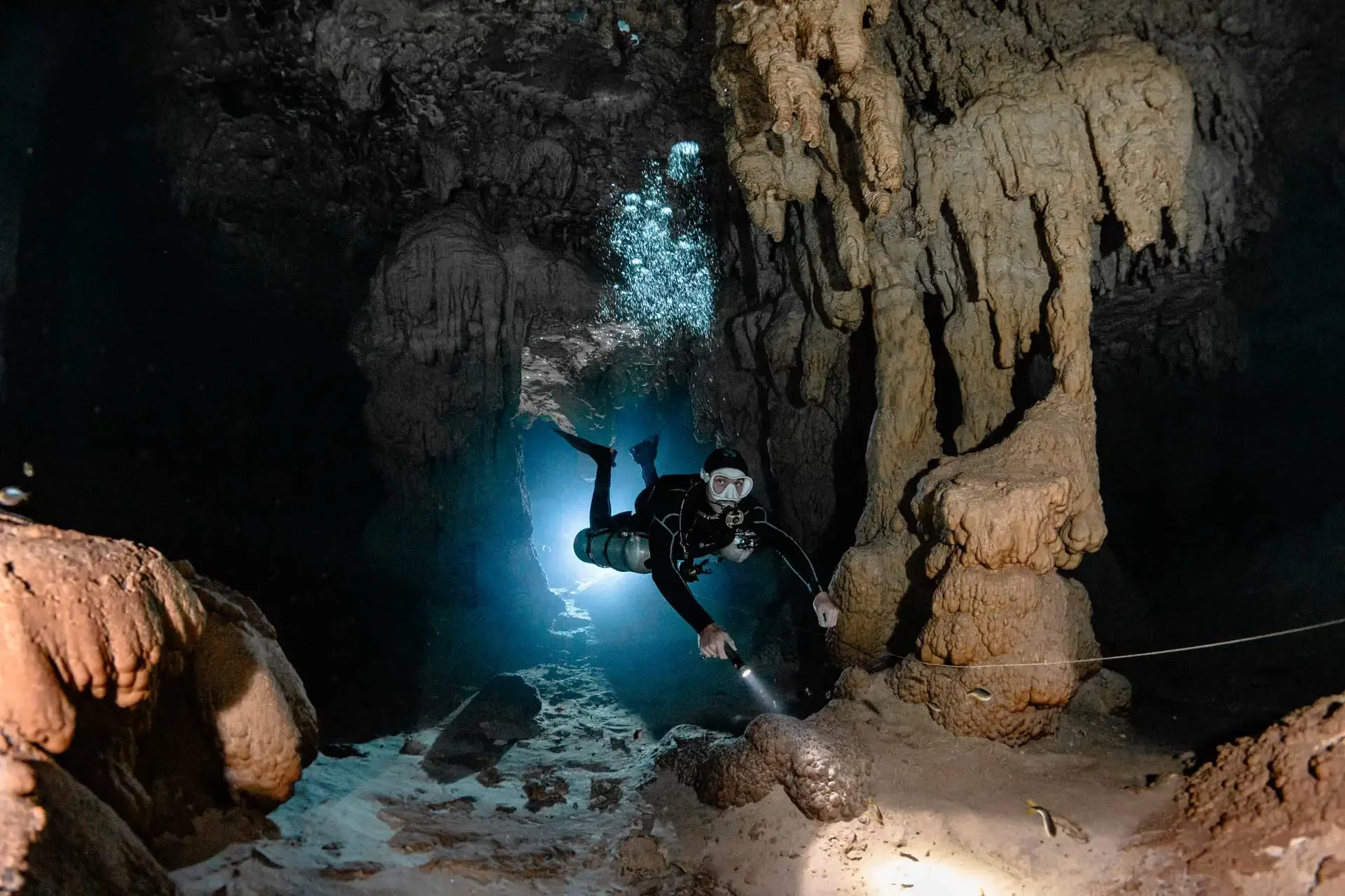 Diver swimming through dense formations toward blue light at Taak Bi Lum cenote