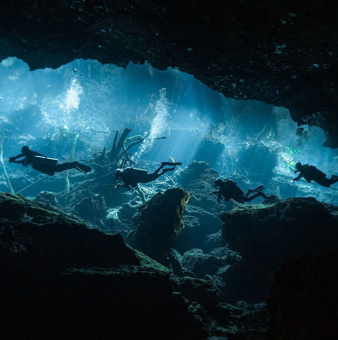 Divers crossing a rocky cavern opening in Chac Mool cenote