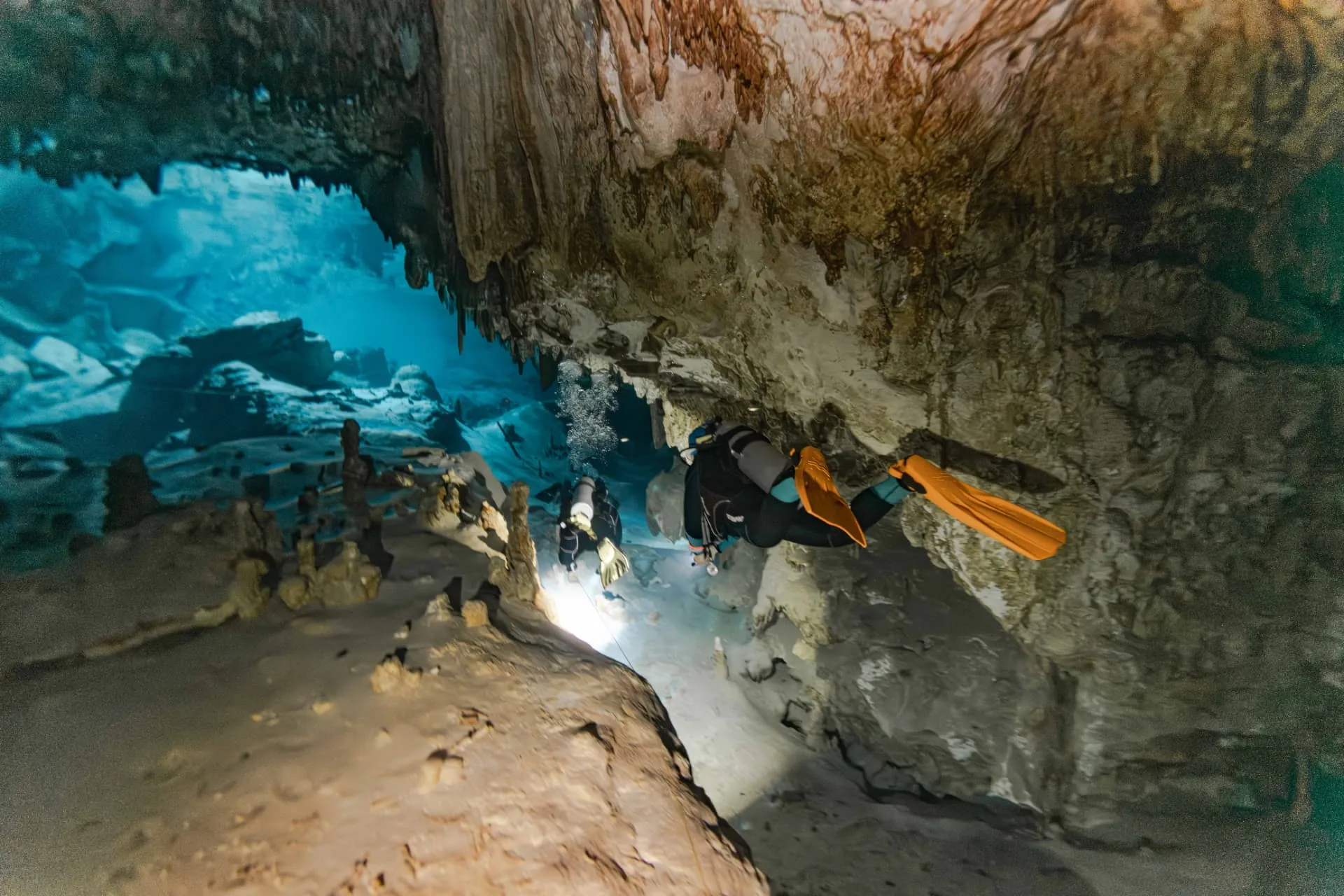 Diver with a light swimming along a cavern passage in Taak Bi Ha cenote.