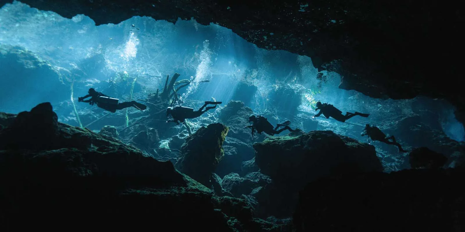 A group of divers crossing beams of natural light inside the Kukulkan cavern