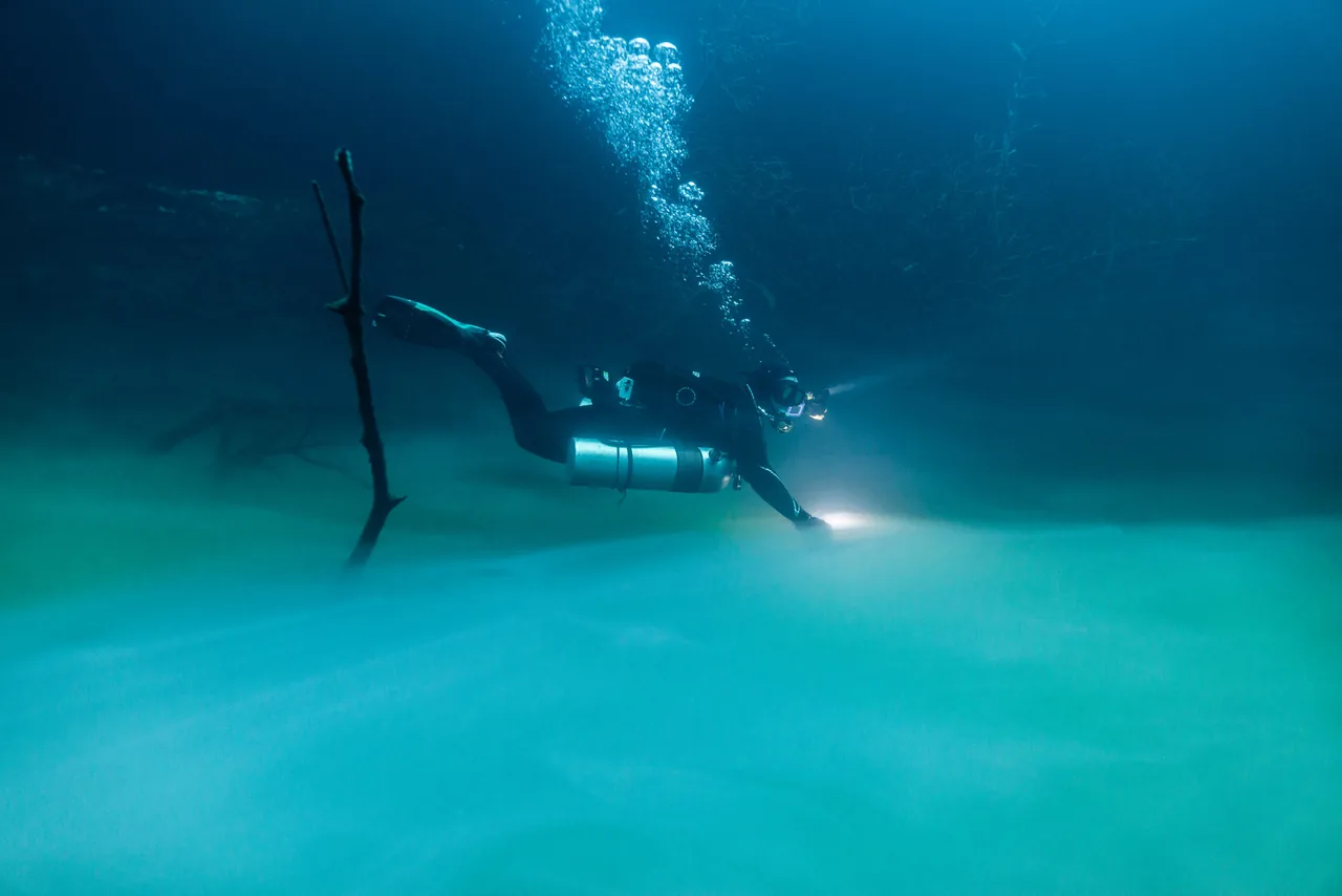 Diver with a light gliding above a dense cloud layer in Cenote Yaakun.