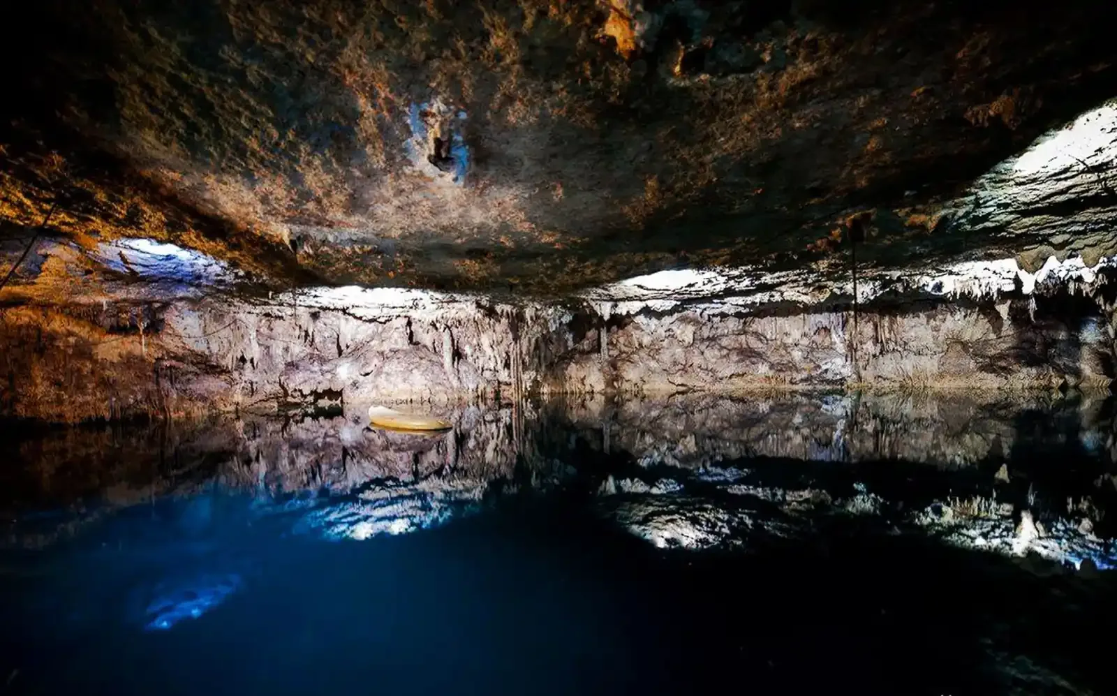Wide limestone chamber reflected in the dark blue water of Kin Ha cenote.