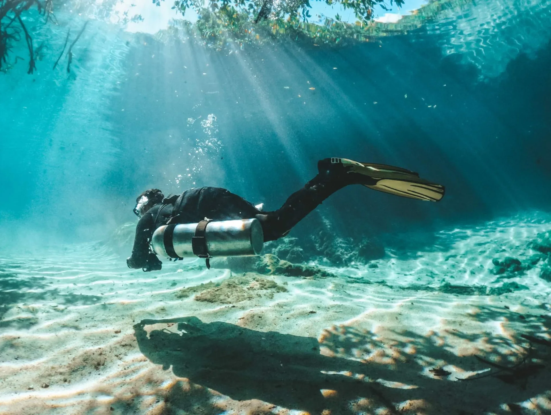 Diver swimming over bright sand in sun rays at Casa Cenote.