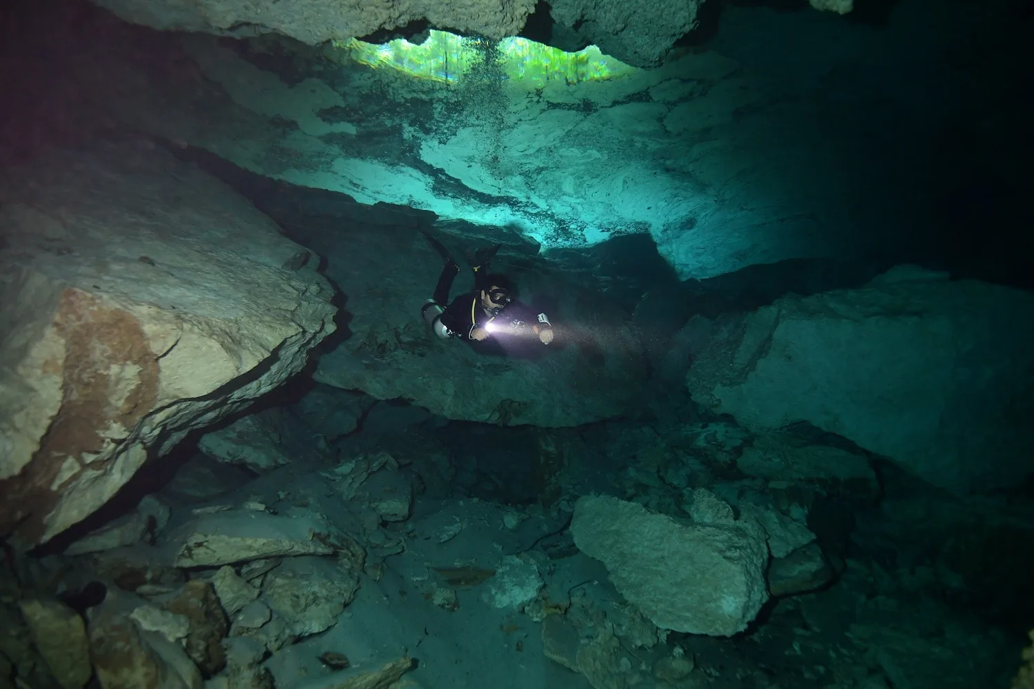 Diver moving through a rocky cavern passage at Chikin Ha cenote.