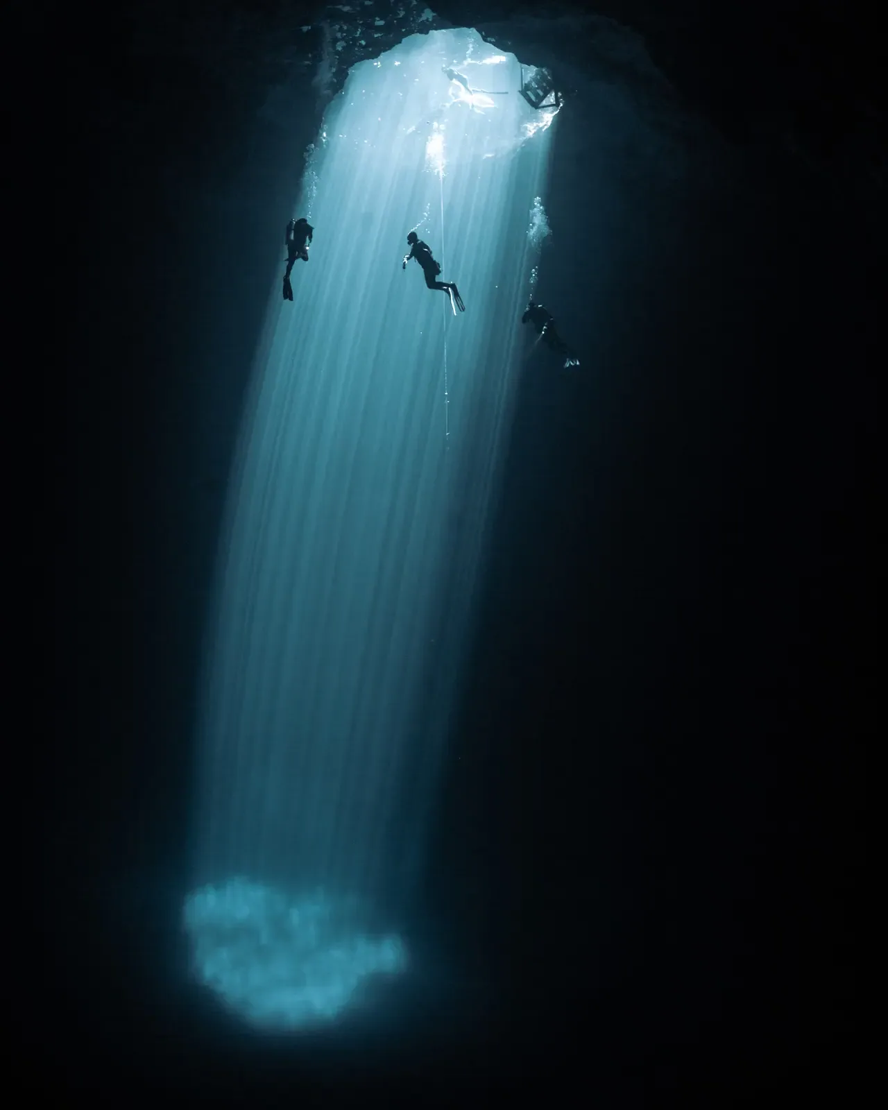 Divers suspended beneath a shaft of natural light in a cenote