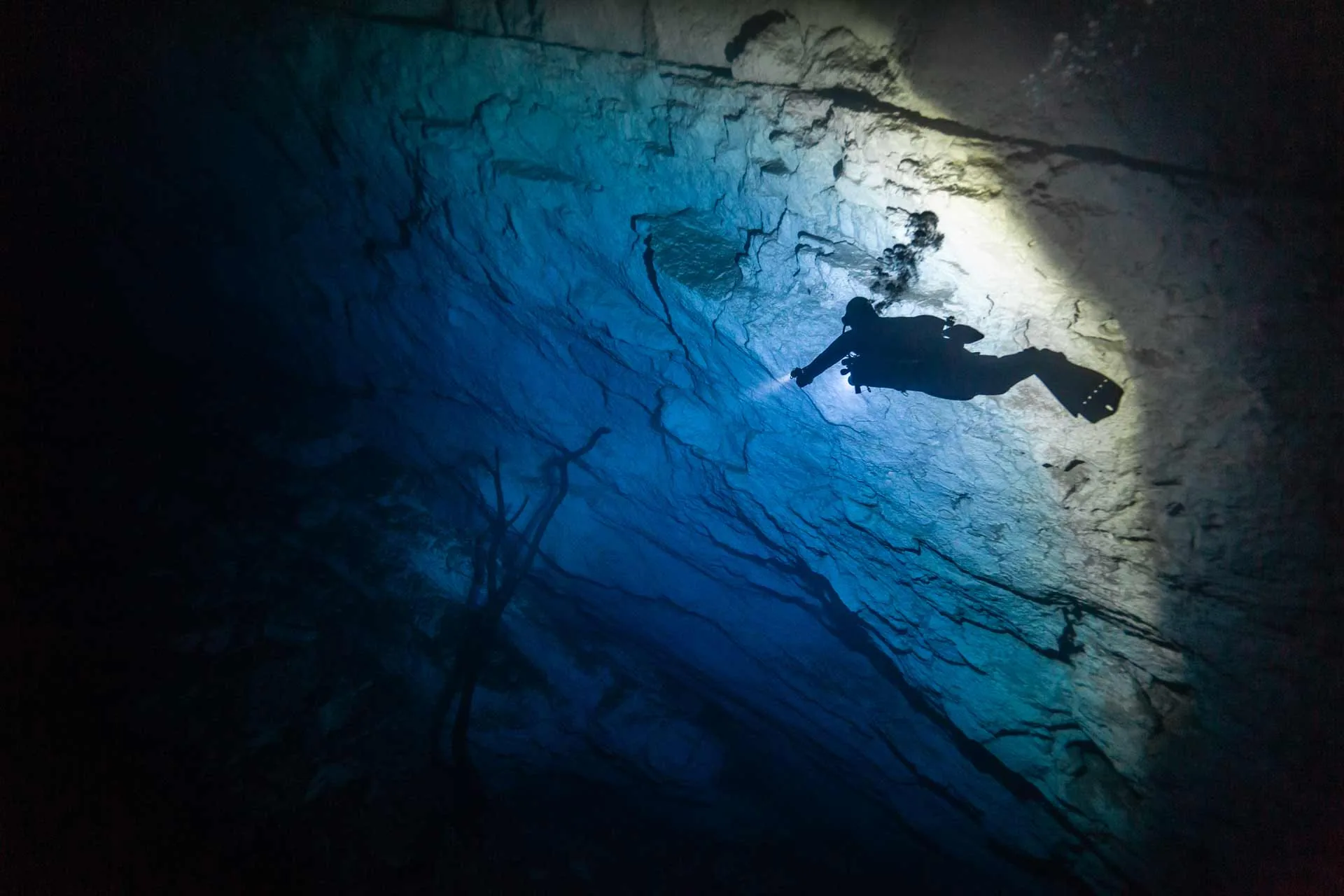 Diver with a light silhouetted along a limestone wall in Cenote Yaakun