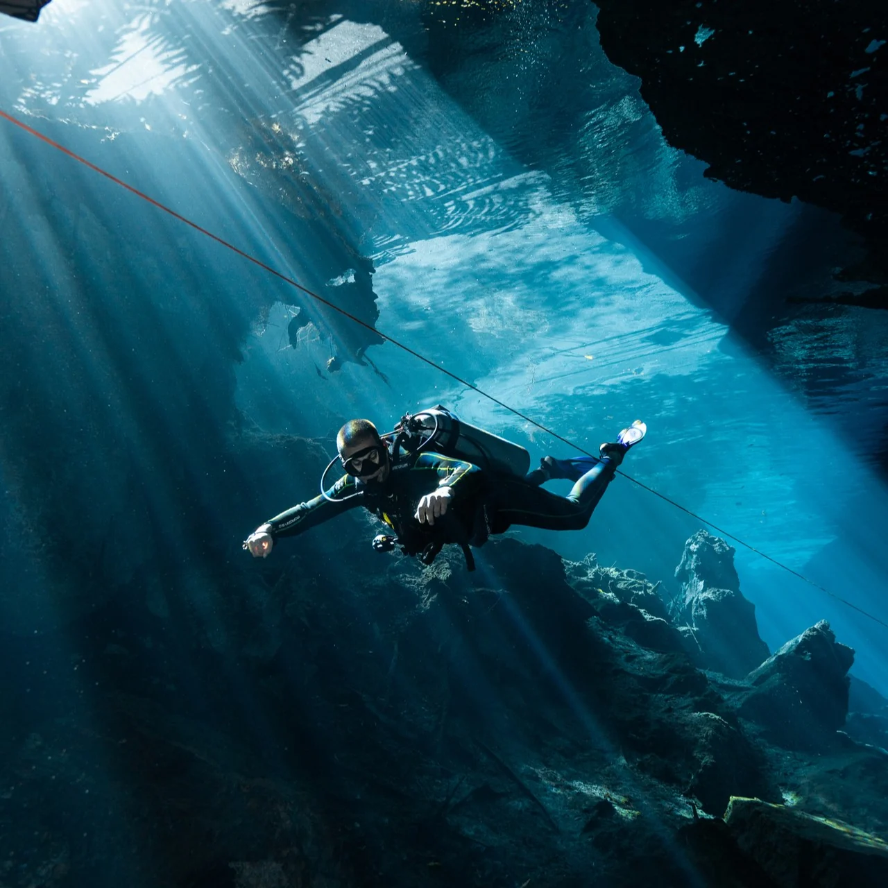 Diver beneath sunbeams inside Kukulkan cenote