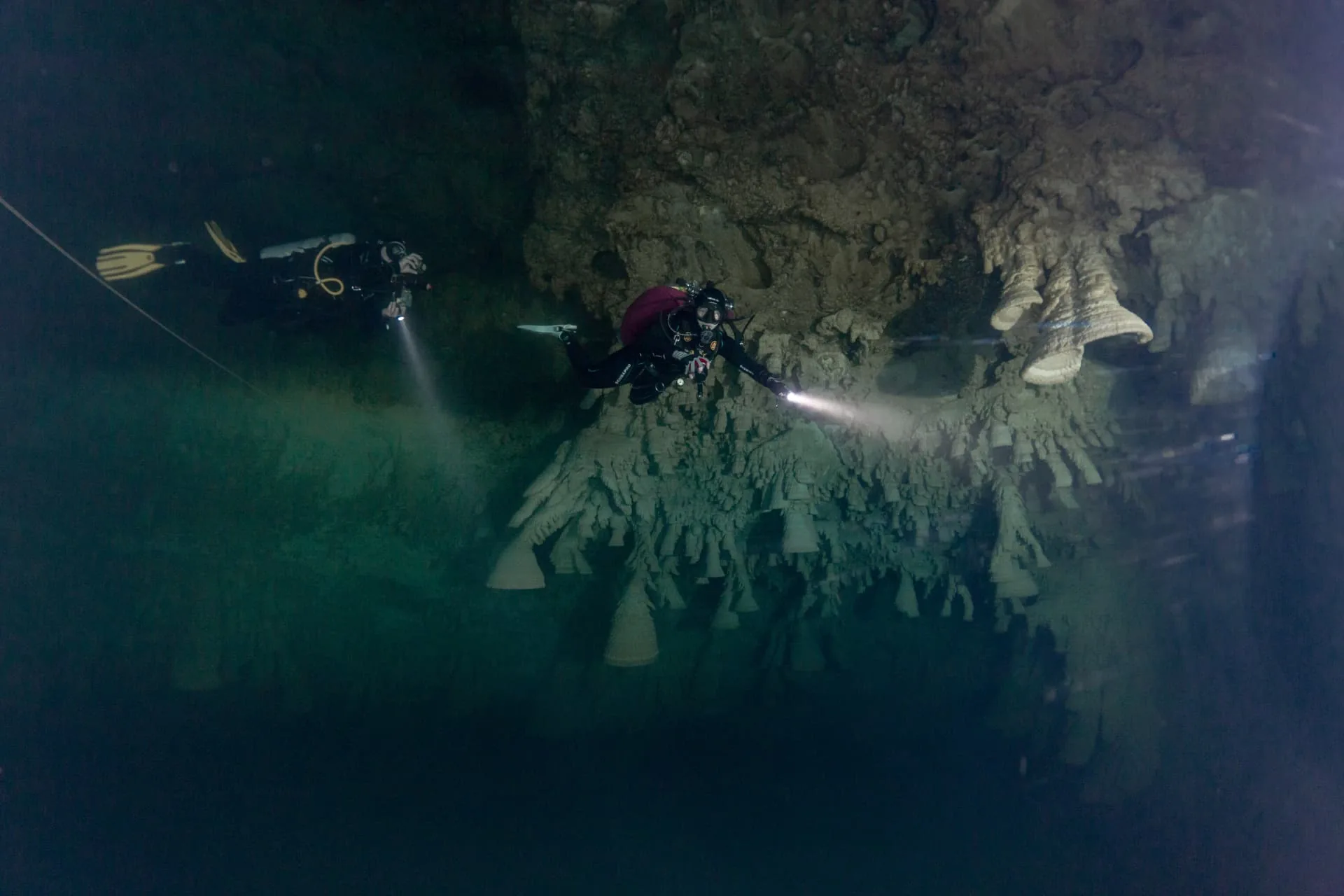 Two divers with lights among the bell-shaped formations of Cenote Zapote