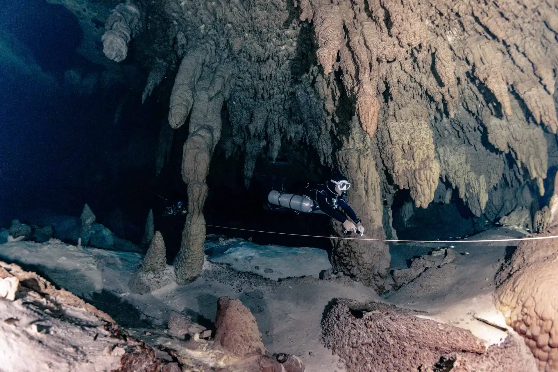 Diver following the guideline between large limestone formations at Taak Bi Lum cenote.