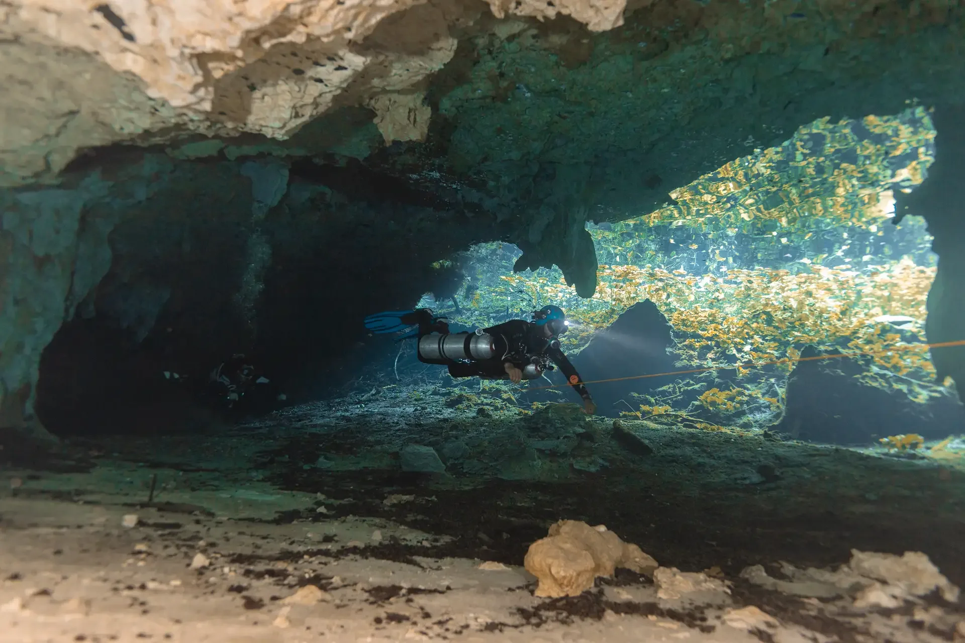 Diver following the guideline beside a sunlit cavern opening at Nicte Ha cenote.