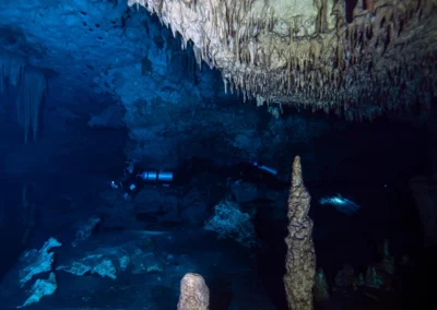 Interior del cenote Dreamgate con buzo avanzando entre columnas de estalactitas y formaciones rocosas