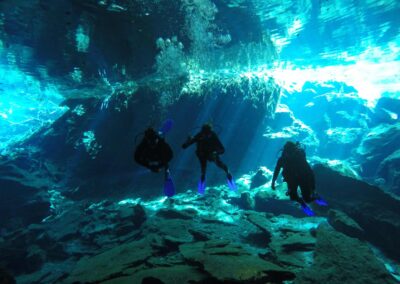 Tres buzos descendiendo en el cenote Chikin Ha bajo luz natural en aguas cristalinas