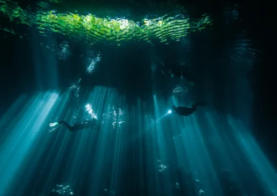 Buzos iluminados por rayos de luz natural descendiendo en el cenote Jardín del Edén – buceo en aguas cristalinas