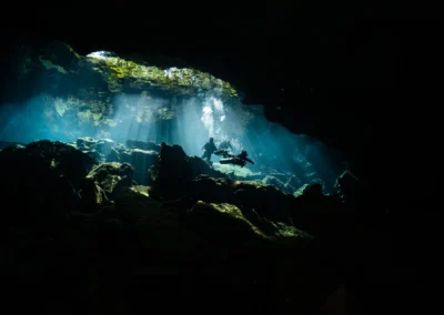 diver illuminated by dramatic sunbeams inside Cenote Kukulkan’s cavern, with stalactites framing the scene