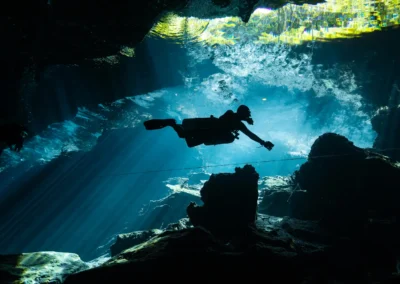 Buzo explorando el Cenote Kukulkán con rayos de luz que atraviesan el agua y estalactitas en primer plano – little brother kukulkan cenote dive