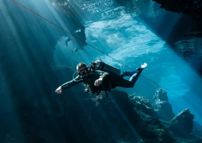 Buzo con equipo completo atravesando haces de luz en el cenote Kukulkan – buceo en caverna con visibilidad cristalina