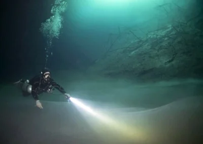 Buzo iluminando con linterna el fondo del cenote Orquídea, con haloclina visible en aguas profundas