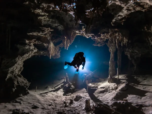 Diver in Cenote Dos Ojos descending into the Bat Cave, surrounded by rock formations.