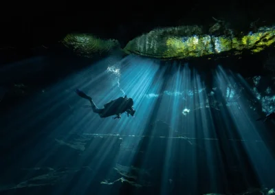 Buzos descendiendo entre haces de luz en el cenote Kukulkan – buceo en aguas cristalinas y cavernas iluminadas