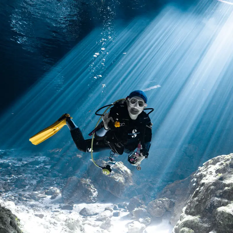Buzo explorando un cenote con rayos de luz en la Riviera Maya
